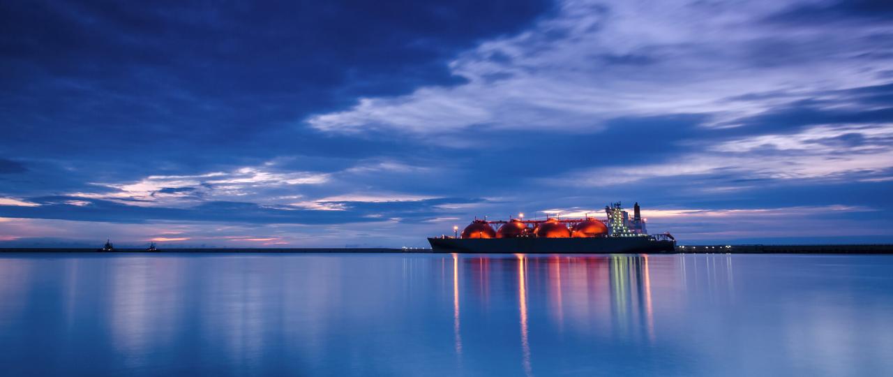 夕暮れの港に海面の高さから見たLNG運搬船Arctic Voyager号の灯りが水面に反射している。