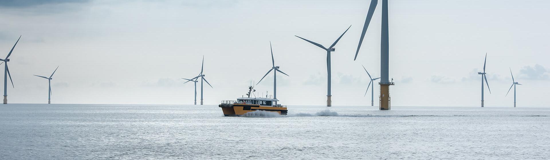 ein Offshore-Windpark. Ein Serviceboot fährt in schnellem Tempo zwischen den Turbinen hindurch und erzeugt dabei Kielwasser.