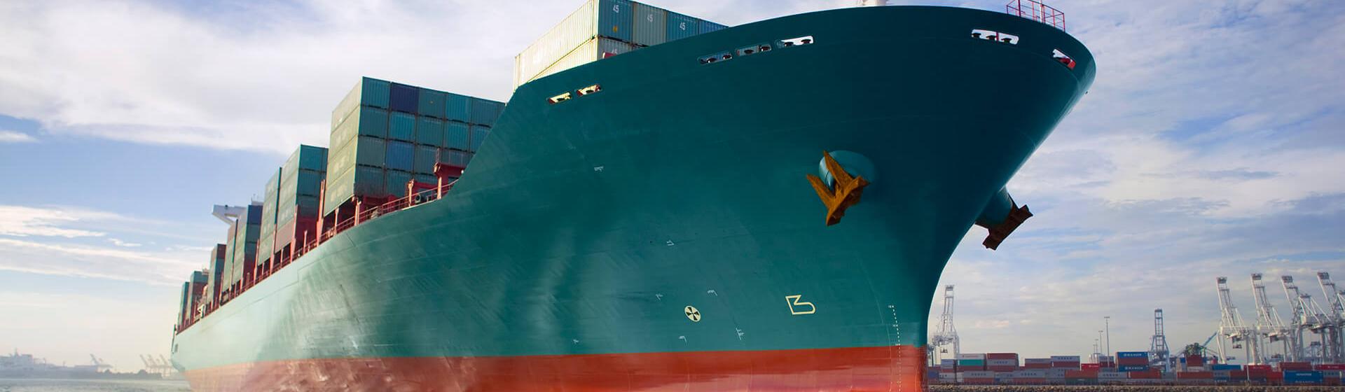 et containerskip som beveger seg gjennom en havn med kraner i bakgrunnen, sett fra havnivå.